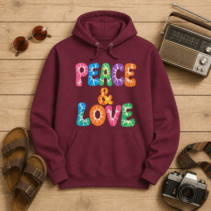Retro tie-dye Peace and Love lettering printed on a black fleece hoodie pullover with vibrant 60s rainbow typography.