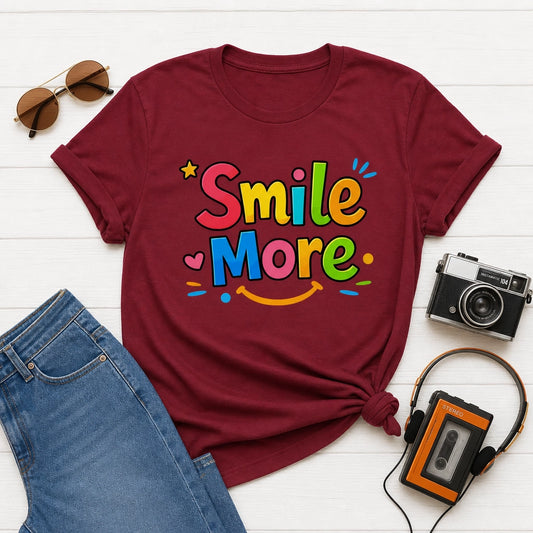 Smile More, bubbly lettering with a yellow sun-smile and pink heart on a black cotton t-shirt.