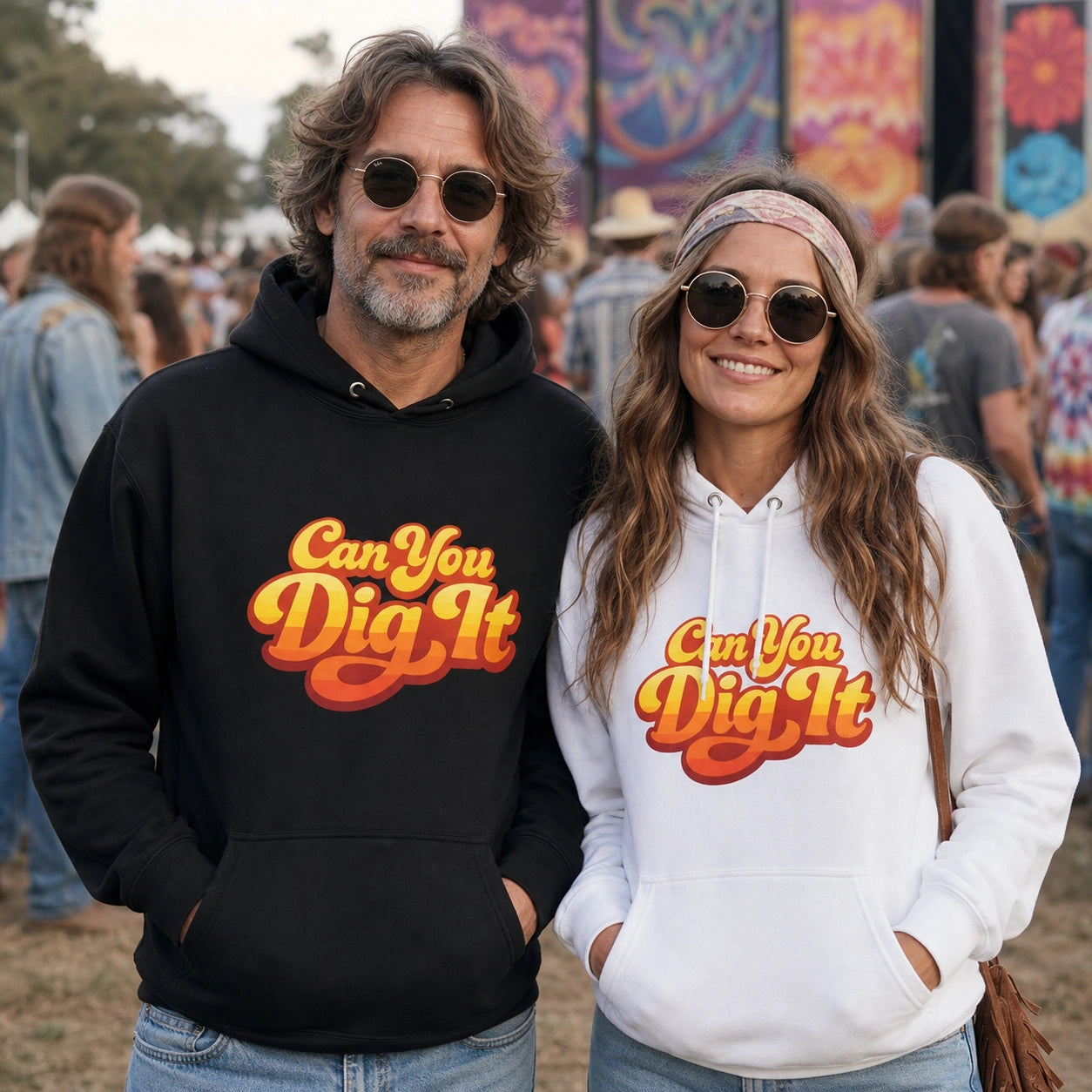 A man and a woman standing outdoors at what looks like a festival or event, each wearing a pullover hoodie with the slogan 'Can You Dig It' in a retro orange and yellow font. The man's hoodie is black, and the woman's is white.