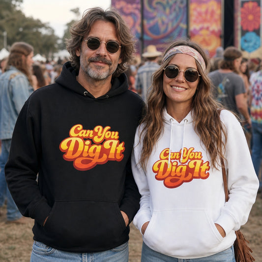 A man and a woman standing outdoors at what looks like a festival or event, each wearing a pullover hoodie with the slogan 'Can You Dig It' in a retro orange and yellow font. The man's hoodie is black, and the woman's is white.