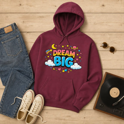 A maroon pullover hoodie with a colorful 'DREAM BIG' graphic on the chest, styled in a flat lay on a light wood background with blue jeans, beige sneakers, sunglasses, and a vinyl record.