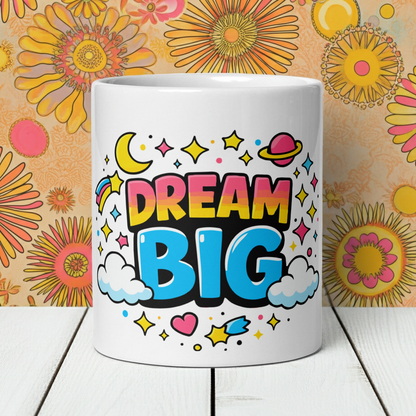 Vibrant "Dream Big" typography with a pink planet, yellow moon, and colorful stars on a black ceramic coffee mug.