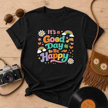 Colorful retro typography reading It’s a Good Day to Be Happy with rainbows, daisies, and stars on a black t-shirt.