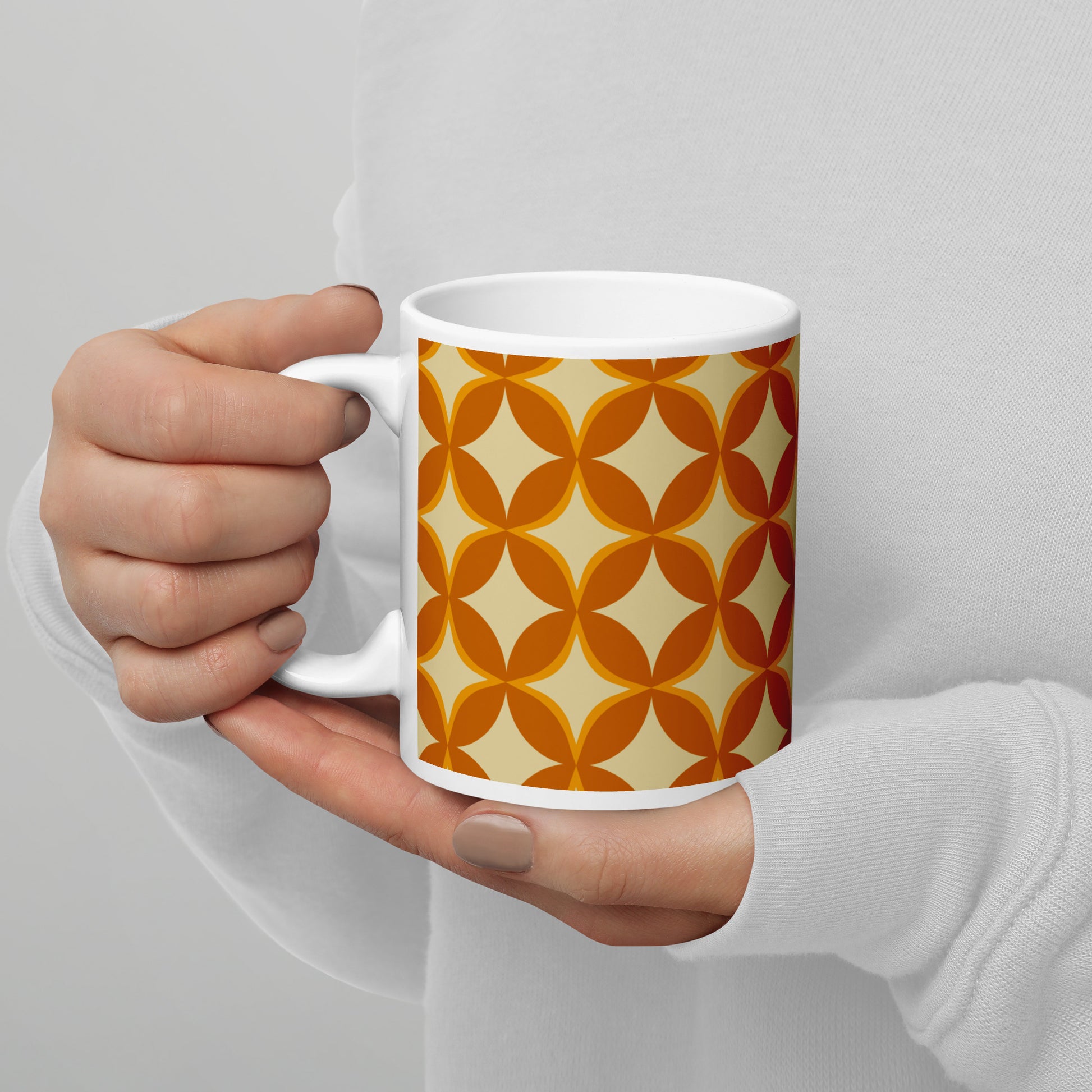 Ceramic coffee mug with a 1970s retro geometric pattern of interlocking orange and mustard petal shapes.