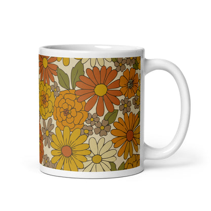 A ceramic coffee mug featuring a seamless retro groovy floral pattern with warm orange, yellow, and cream daisy blooms.