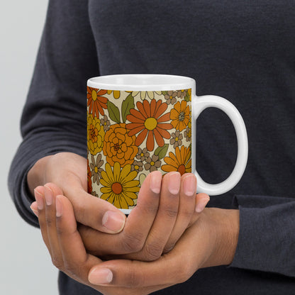 A ceramic coffee mug featuring a seamless retro groovy floral pattern with warm orange, yellow, and cream daisy blooms.