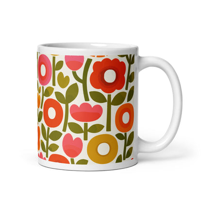 Retro 1970s flower power pattern ceramic mug featuring geometric orange, pink, and yellow flowers with green leaves
