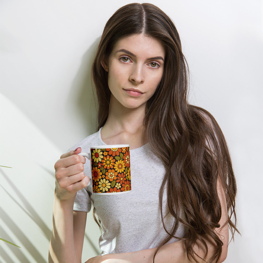 Retro 70s floral pattern ceramic mug featuring orange, yellow, and cream daisies on a dark brown background.