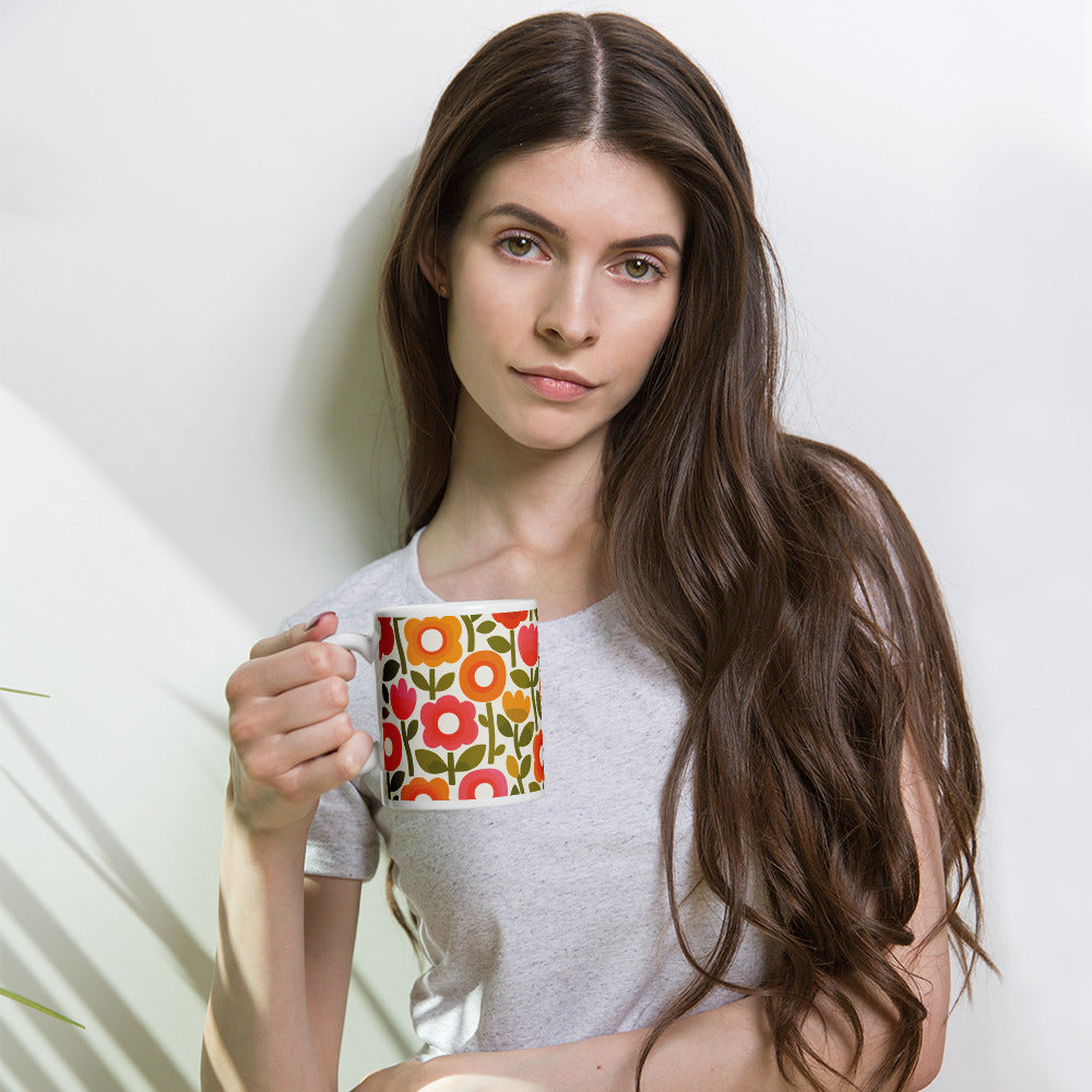 Retro 1970s flower power pattern ceramic mug featuring geometric orange, pink, and yellow flowers with green leaves