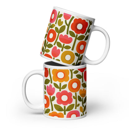 Retro 1970s flower power pattern ceramic mug featuring geometric orange, pink, and yellow flowers with green leaves